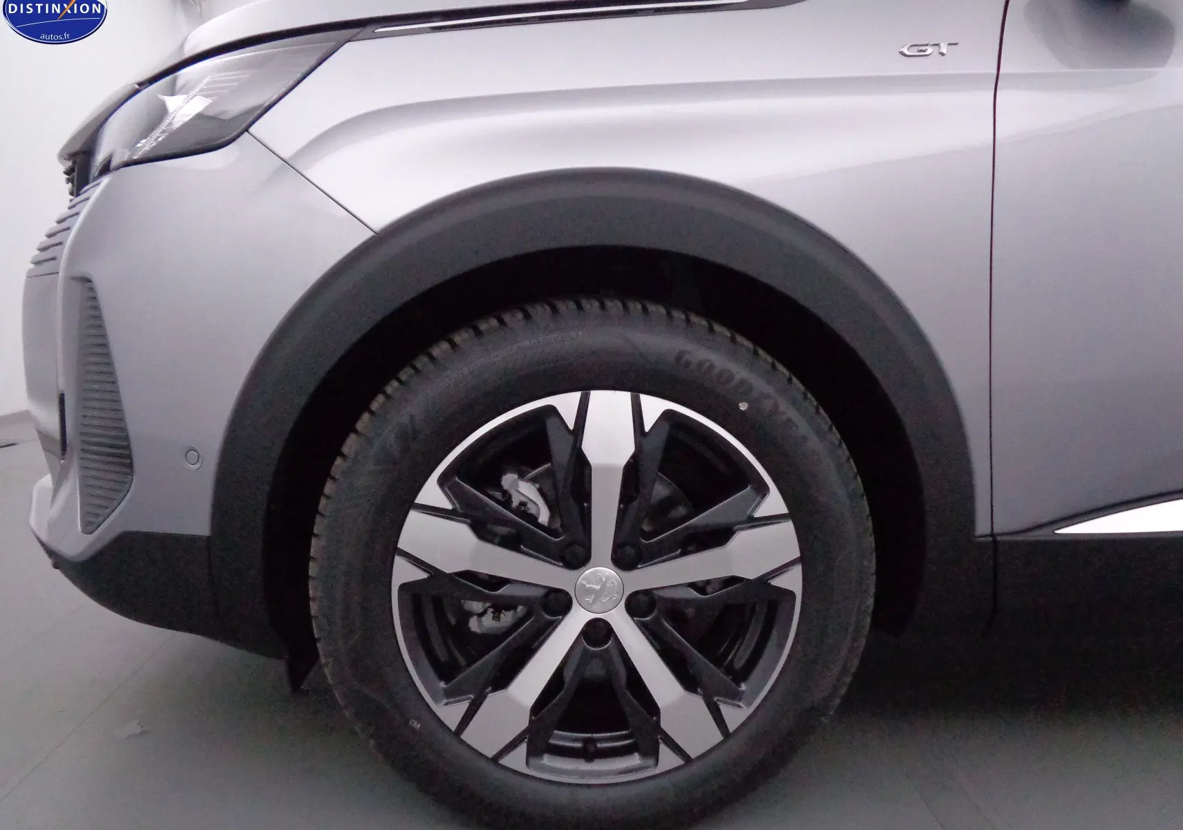Gros plan sur la roue avant gauche d'un Peugeot 3008 gris Artense Métal avec badge GT visible sur l'aile.