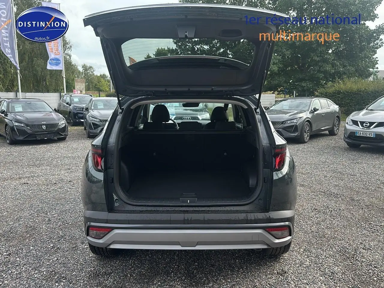 Vue arrière d'un Hyundai Tucson vert cyprès 2025 avec coffre ouvert sur un parking multimarque.