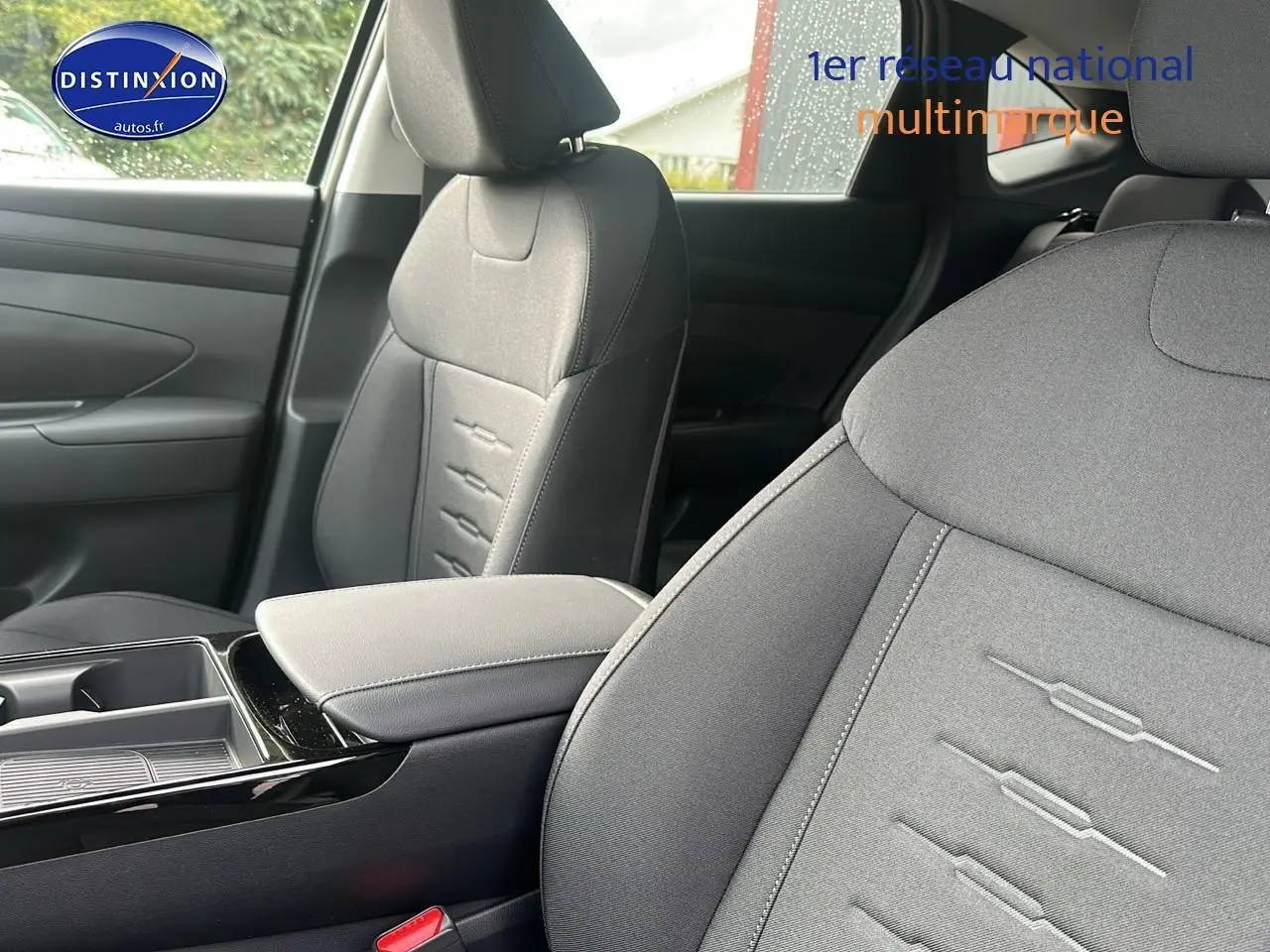 Gros plan sur les sièges avant gris du Hyundai Tucson 2025, mettant en valeur les surpiqûres et l'accoudoir central.