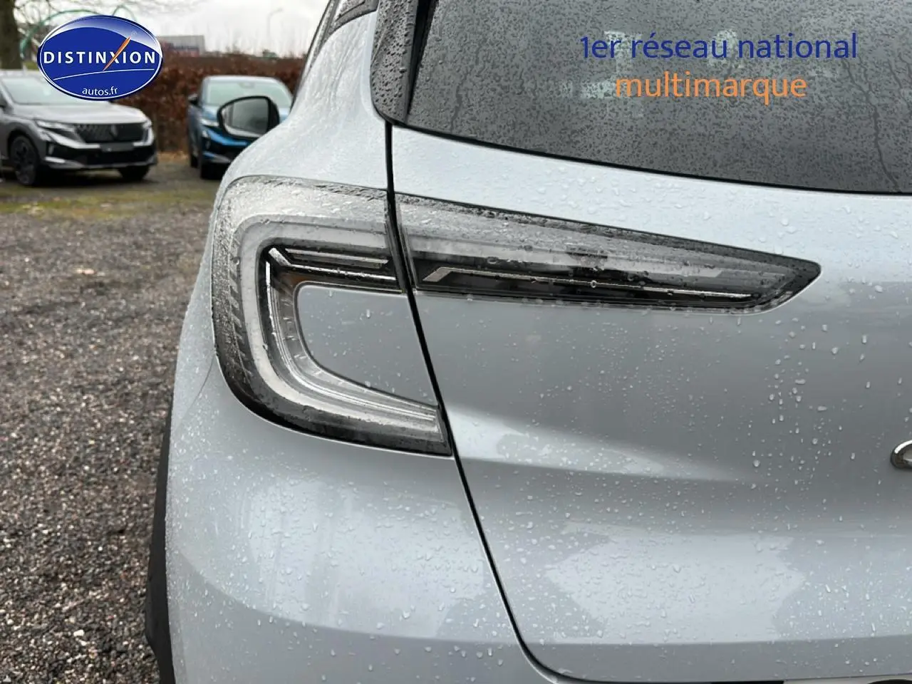 Gros plan sur le feu arrière gauche du Renault Captur gris rafale 2026 sous la pluie, avec logo partiel visible.