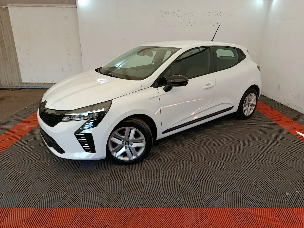 Renault Clio blanche vue 3/4 avant droit, avec jantes alliage et rétroviseurs noirs dans un intérieur lumineux.