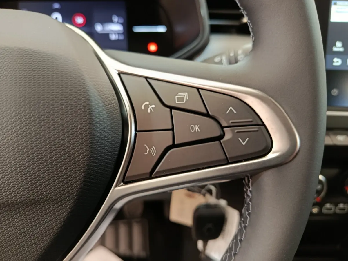 Gros plan sur les commandes multifonctions à droite du volant cuir de la Renault Clio blanche 2024, avec affichage numérique en arrière-plan.
