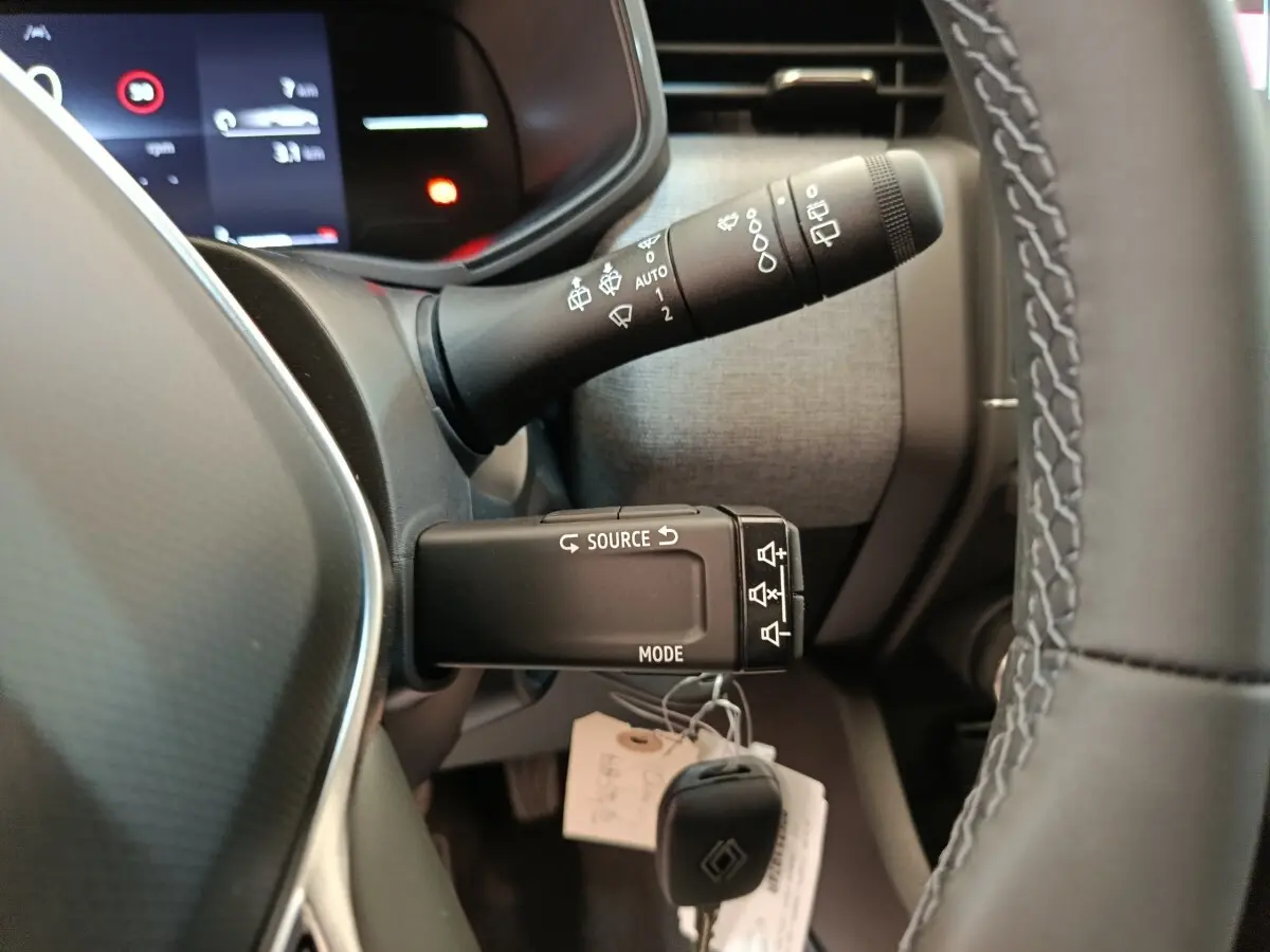 Gros plan sur les commandes au volant et le combiné d'instruments d'une Renault Clio blanche 2024, intérieur moderne.