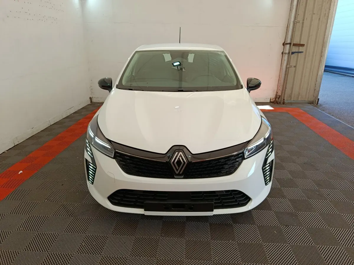 Vue avant d'une Renault Clio blanche 2024 avec calandre noire et feux LED allumés dans un garage.