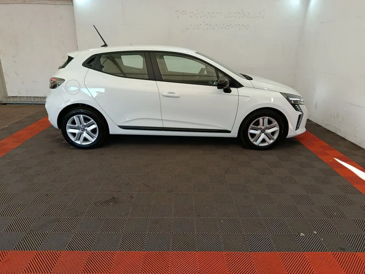 Renault Clio blanc vue de profil côté gauche dans un garage avec éclairage intérieur et sol à damier noir et rouge.