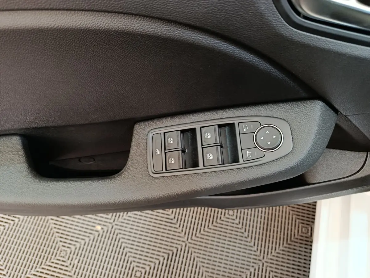 Vue rapprochée de la commande des vitres électriques et rétroviseurs sur la porte côté conducteur d'une Renault Clio blanche 2024.