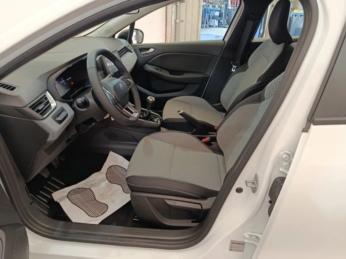 Intérieur de la Renault Clio blanc 2024, vue côté conducteur, sièges gris et tableau de bord moderne avec écran tactile.