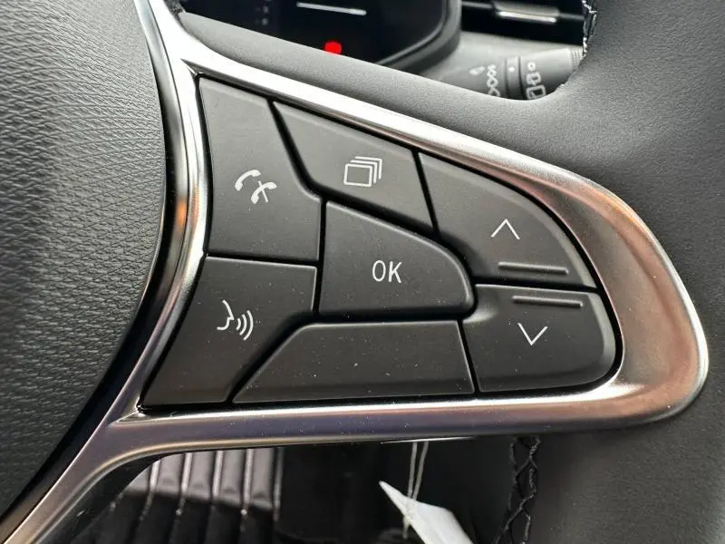 Gros plan sur les commandes multifonctions à droite du volant d’une Renault Clio gris 2025, boutons noirs avec cadre argenté.