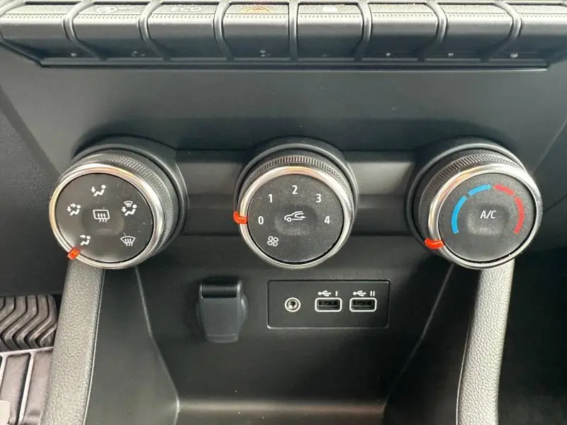 Gros plan sur les commandes de climatisation et ventilation noires avec touches rouges, prises USB et prise jack sur Renault Clio gris 2025.