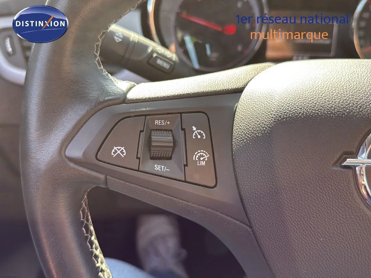 Gros plan sur les commandes de régulateur de vitesse au volant en cuir noir de l'Opel Astra Sports Tourer gris minéral.