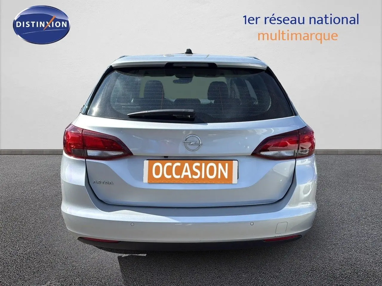 Vue arrière d'une Opel Astra Sports Tourer gris minéral métal avec feux rouges et plaque "OCCASION" visible.