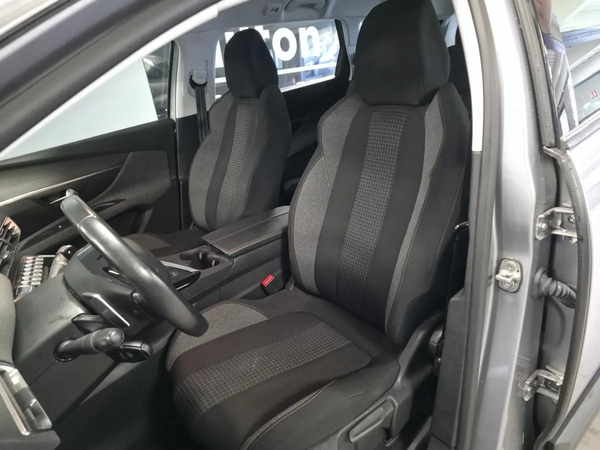 Vue intérieure côté conducteur du Peugeot 5008 gris 2020, sièges tissu bicolore avec accoudoir central ouvert.
