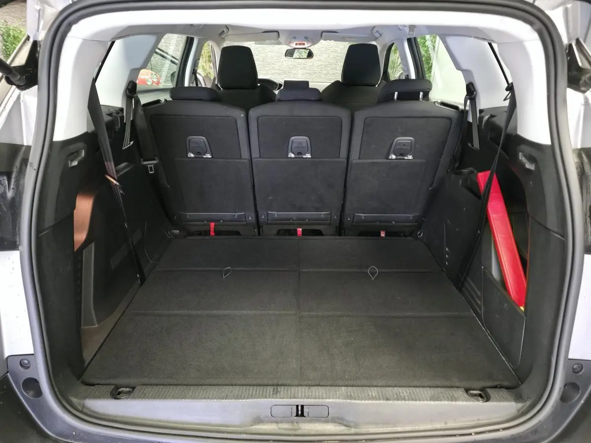 Coffre ouvert vu de l'arrière d'un Peugeot 5008 gris, sièges arrière relevés et plancher de coffre plat.