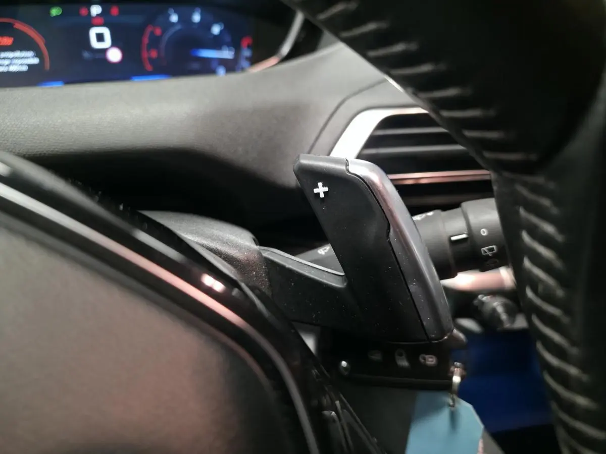 Gros plan sur la palette de changement de vitesse droite du volant d'une Peugeot 5008 gris, tableau de bord en arrière-plan flou.