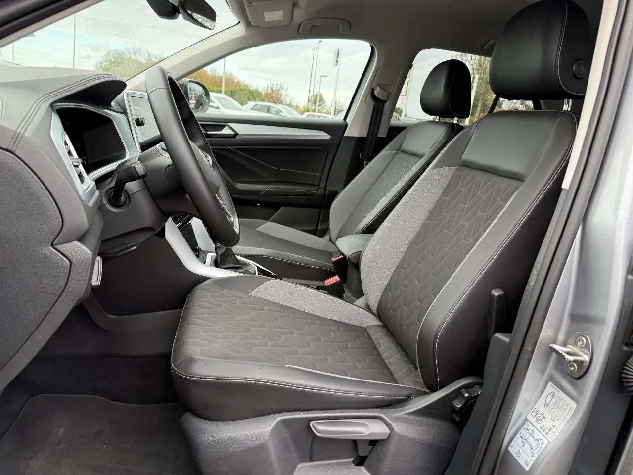 Intérieur côté conducteur du Volkswagen T-Roc argent, montrant les sièges avant en tissu et cuir avec console centrale.