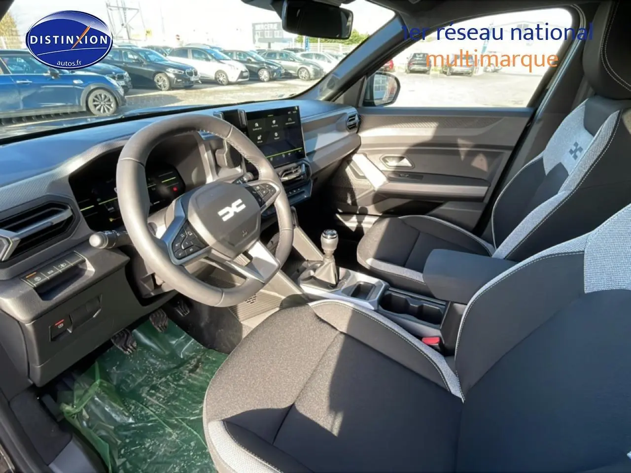 Vue intérieure côté conducteur du Dacia Duster 2026, sièges bi-ton gris et noir avec volant multifonction et boîte manuelle.