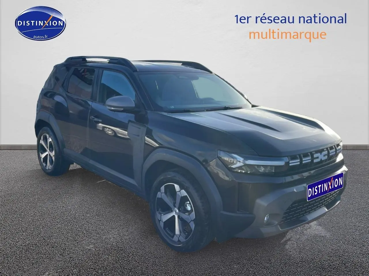 Dacia Duster noir en 3/4 avant droit, avec jantes alu et barres de toit visibles sur fond neutre.