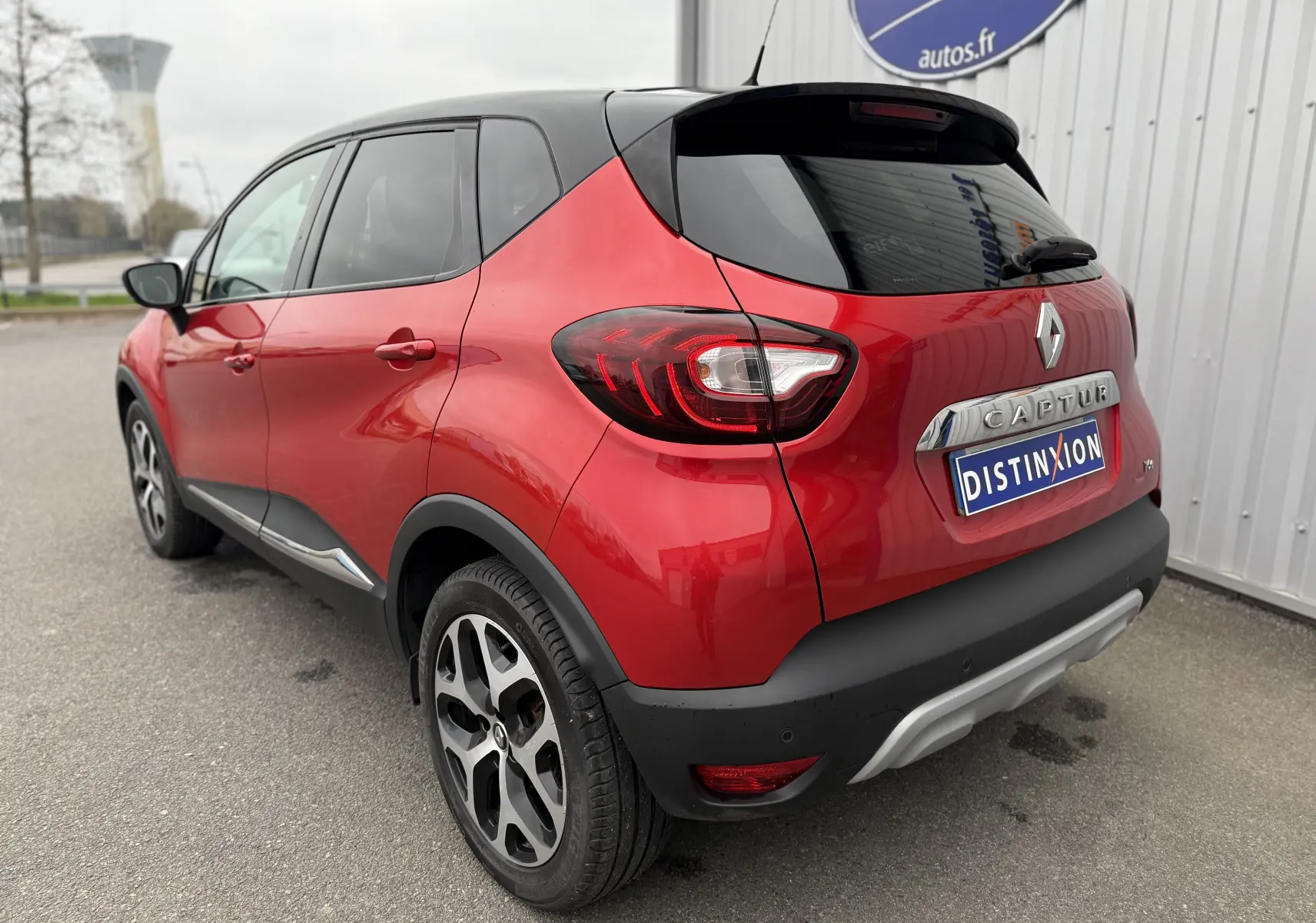 Vue 3/4 arrière droite d'un Renault Captur rouge 2017 avec toit noir et jantes alliage bicolores.