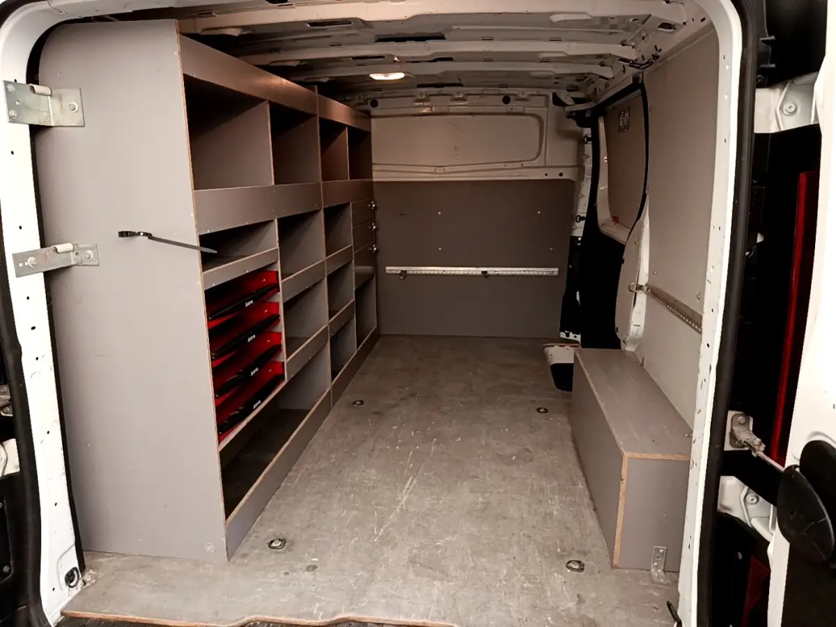 Vue intérieure arrière du Renault Trafic Fourgon blanc avec aménagements de rangement gris sur le côté gauche.