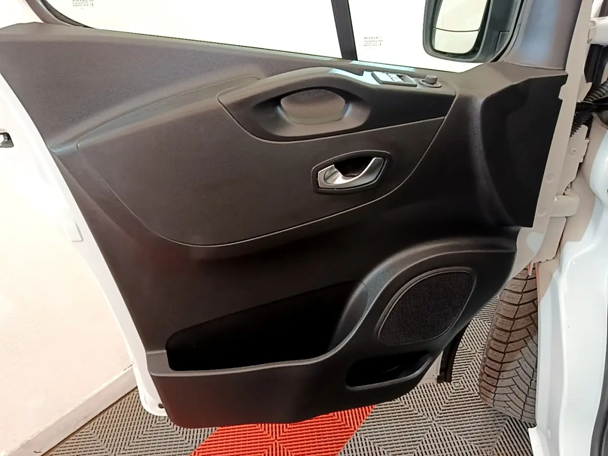 Vue rapprochée de la porte avant droite noire du Renault Trafic Fourgon blanc, avec poignée et haut-parleur intégrés.
