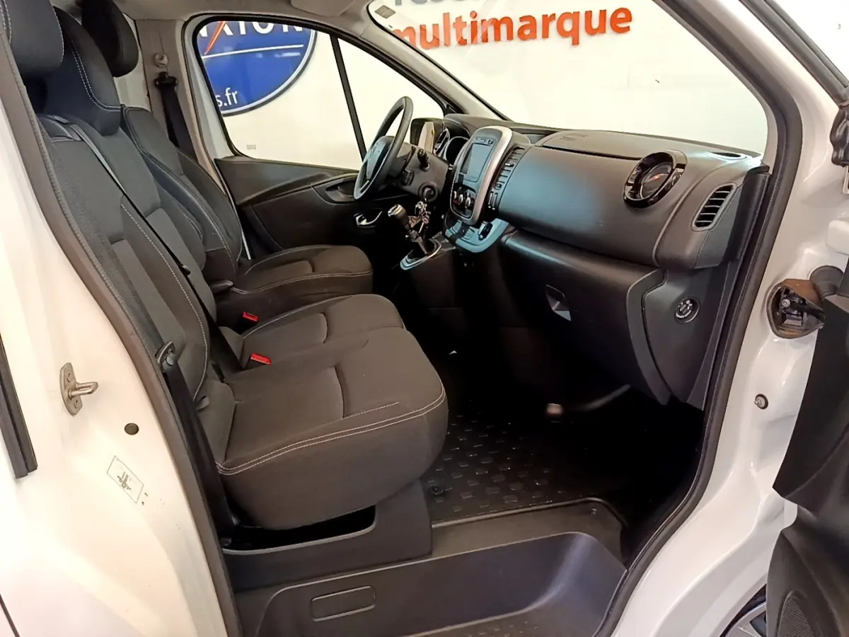 Intérieur côté conducteur du Renault Trafic blanc, montrant les sièges avant, tableau de bord et volant réglable.