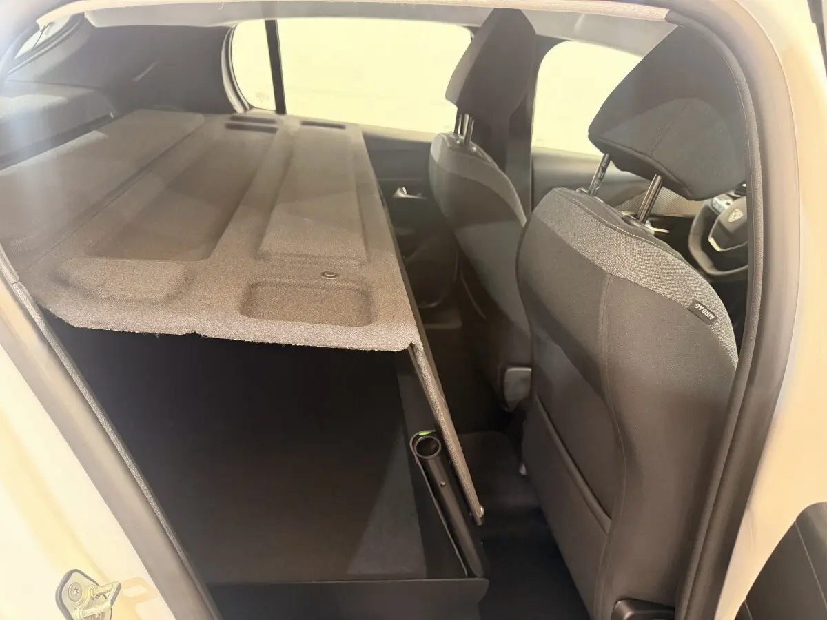 Vue intérieure côté droit de la Peugeot 208 blanche 2025, montrant les sièges avant et le coffre avec cache-bagages relevé.
