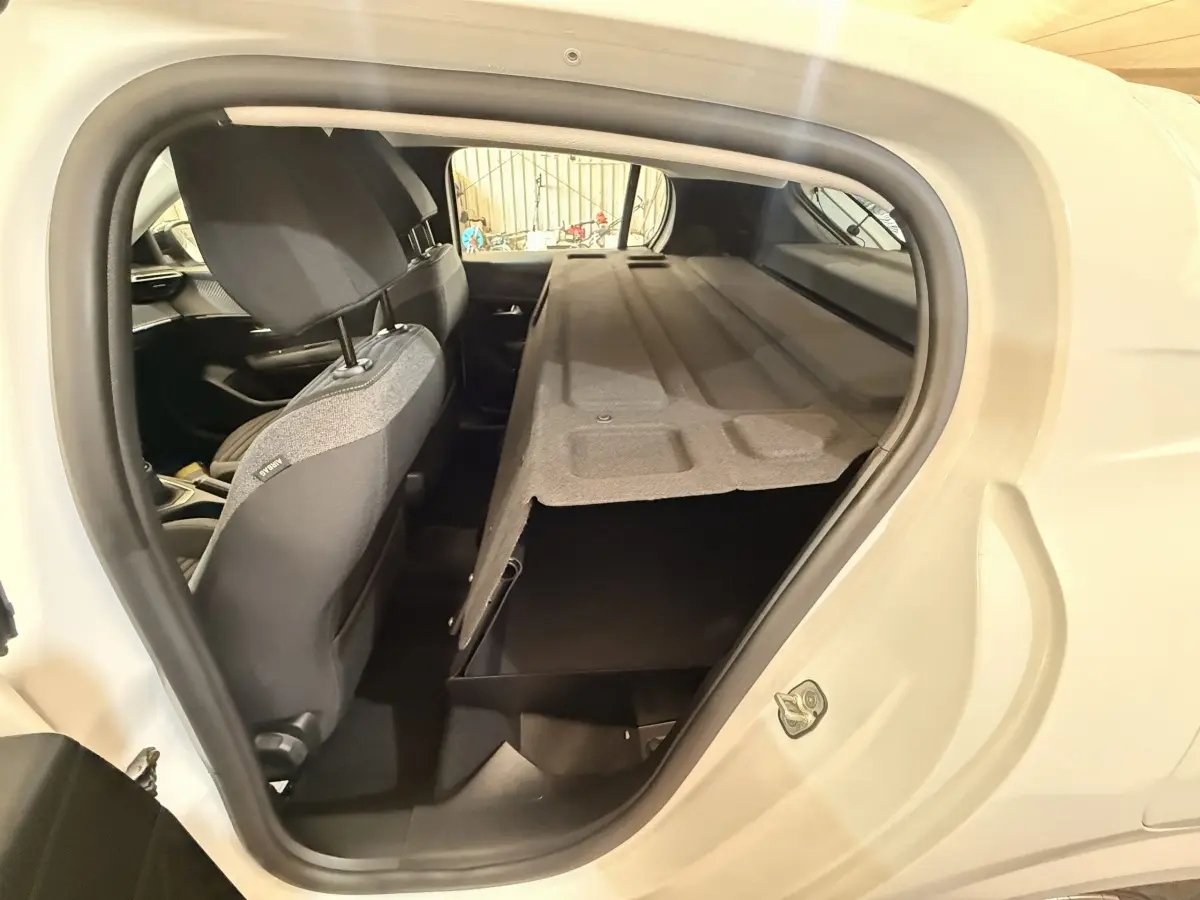 Vue intérieure côté gauche du coffre ouvert d'une Peugeot 208 blanche, avec banquette arrière rabattue.