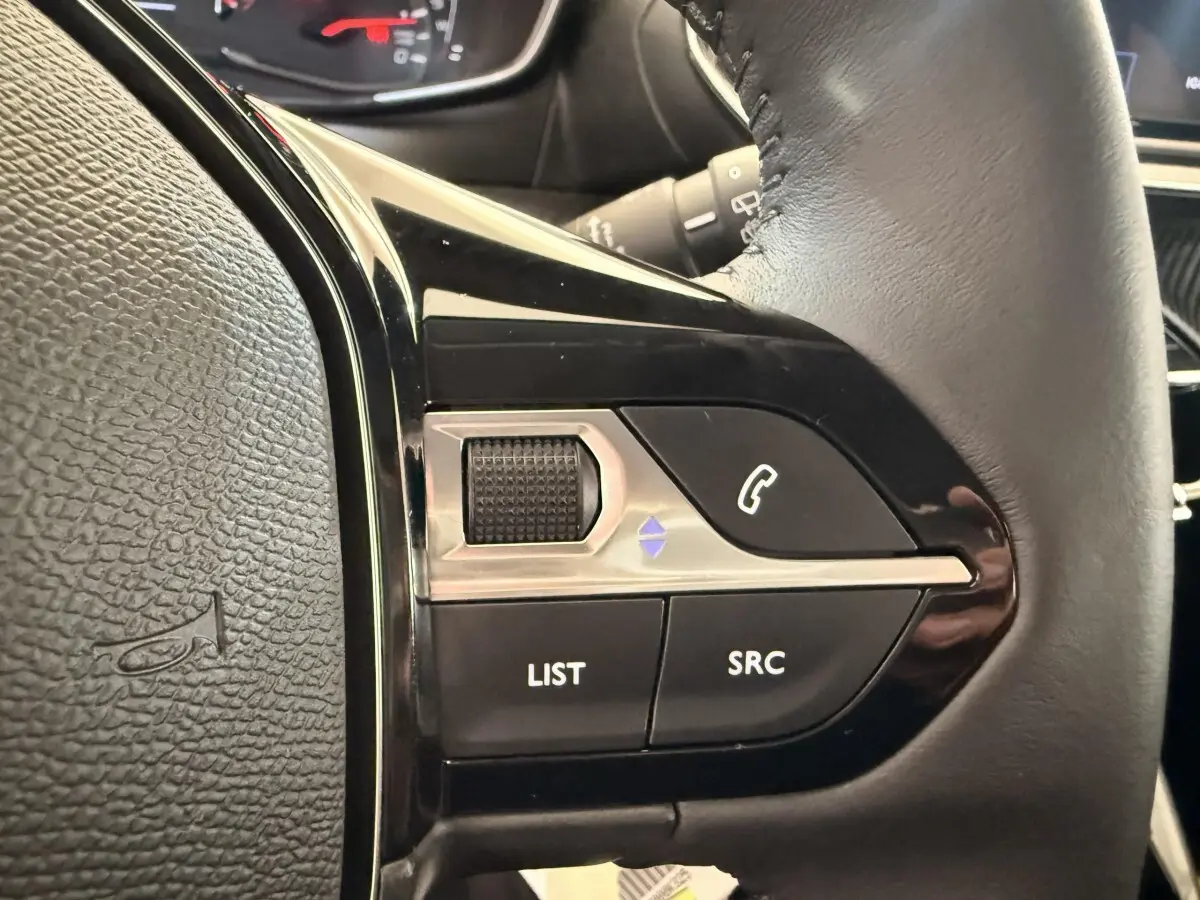 Gros plan sur les commandes gauche du volant cuir noir de la Peugeot 208 2025, avec boutons LIST, SRC et téléphone.