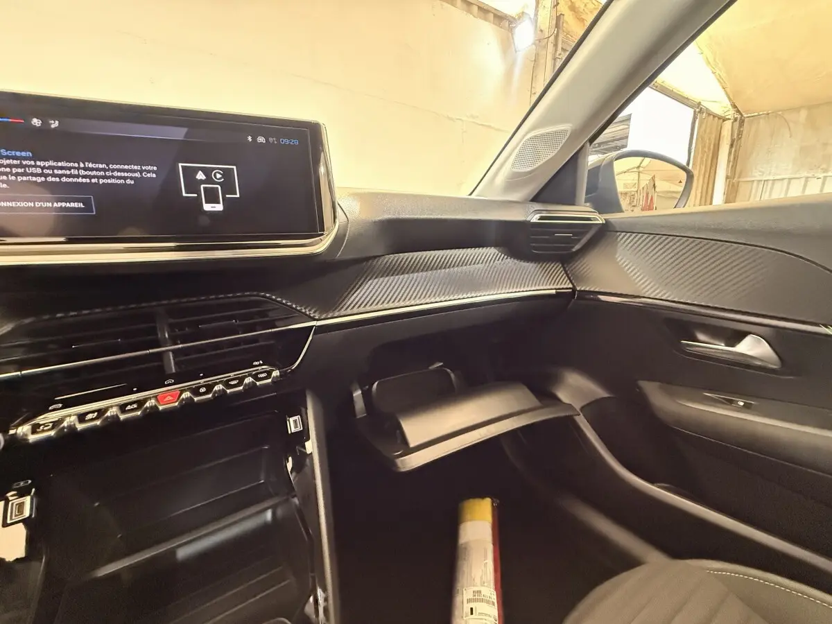 Intérieur de la Peugeot 208 blanc, vue côté passager, tableau de bord moderne avec écran tactile et boîte à gants ouverte.