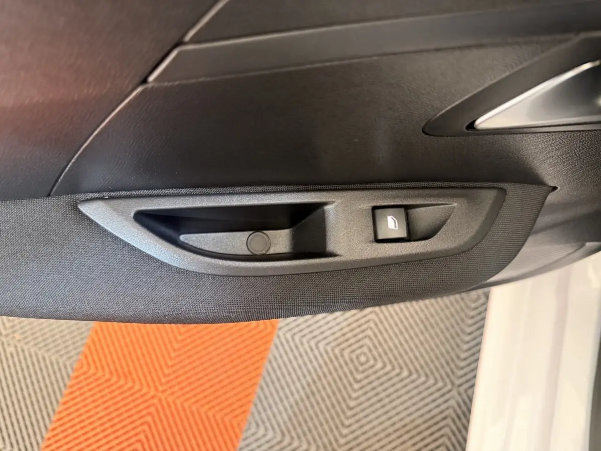 Gros plan sur la commande de lève-vitre côté conducteur d’une Peugeot 208 blanche, intérieur noir.
