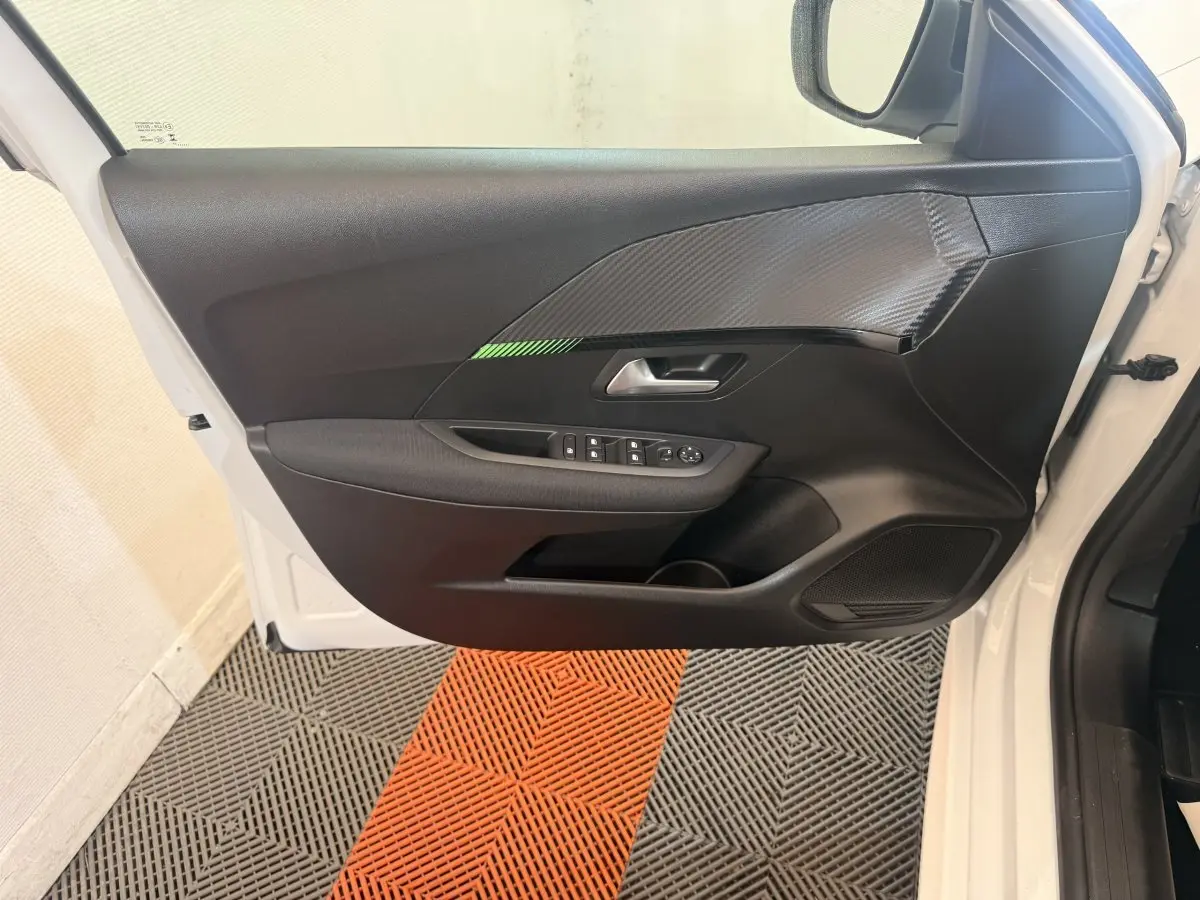 Vue intérieure de la porte avant gauche blanche de la Peugeot 208 2025 avec insert noir texturé et commandes électriques.