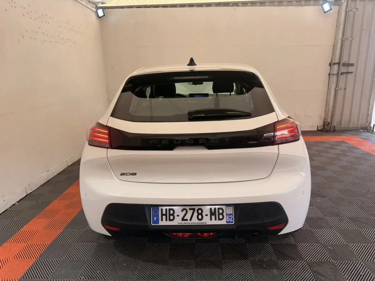 Vue arrière d'une Peugeot 208 blanche 2025 garée en intérieur avec feux arrière allumés et plaque d'immatriculation française.