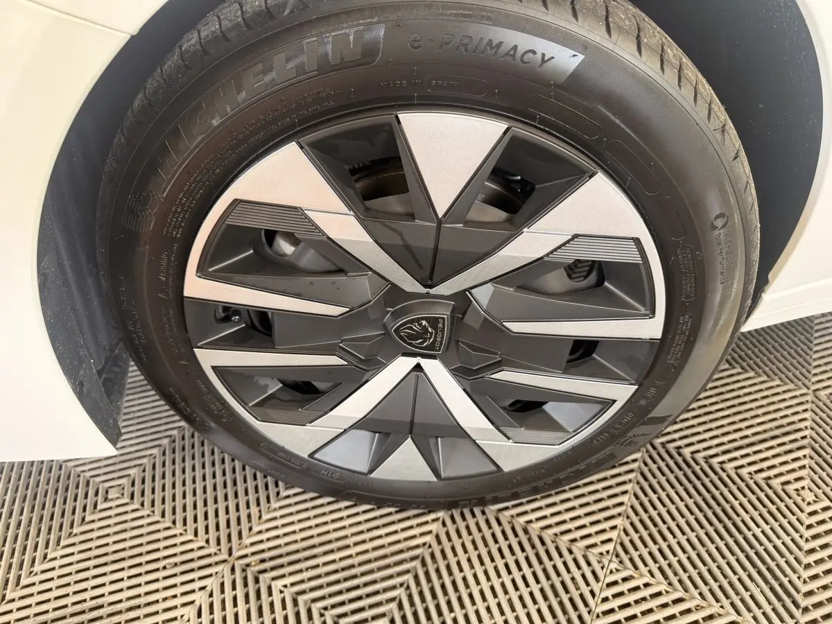 Gros plan sur la roue avant droite blanche d'une Peugeot 208 2025 avec jante au design géométrique noir et argent.