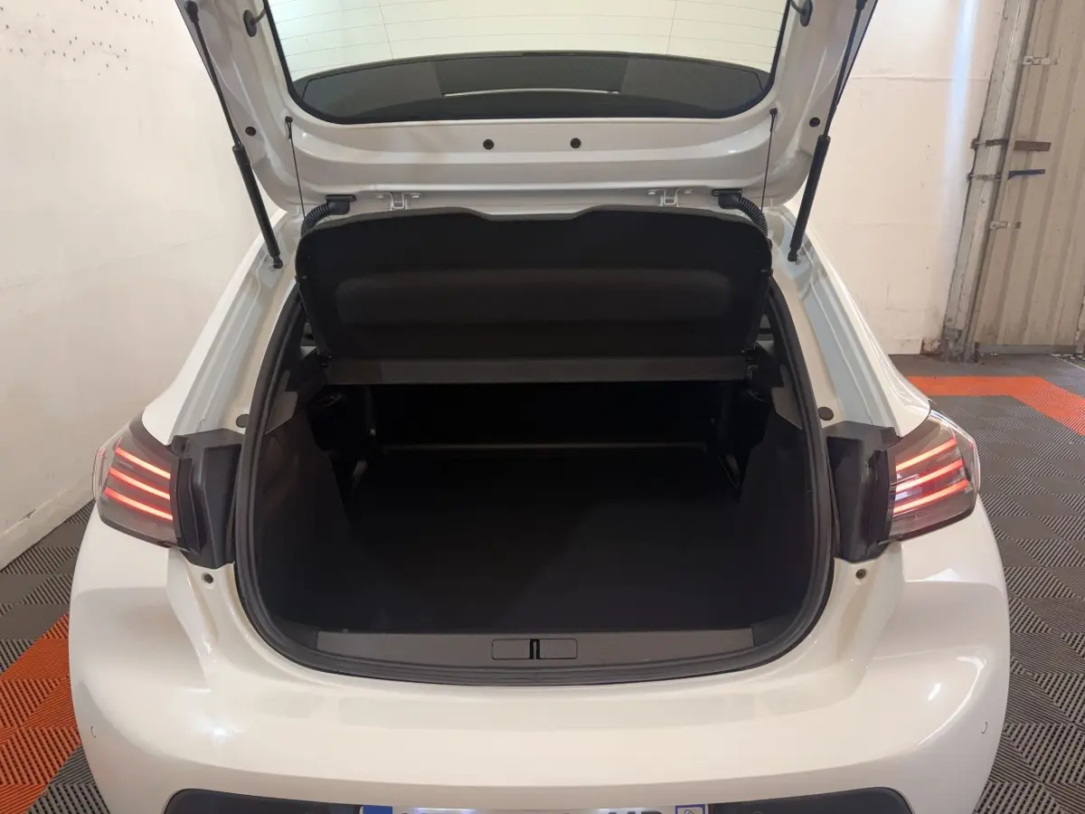 Vue arrière ouverte du coffre d'une Peugeot 208 blanche 2025, avec feux arrière allumés et intérieur de coffre vide.