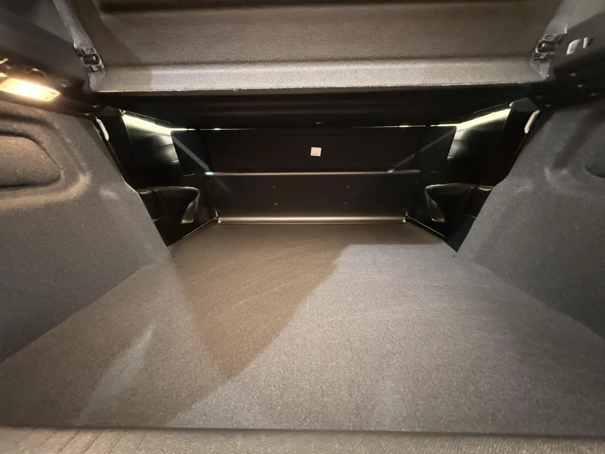 Coffre ouvert d’une Peugeot 208 blanche, vue intérieure montrant l’espace de chargement et la moquette grise.