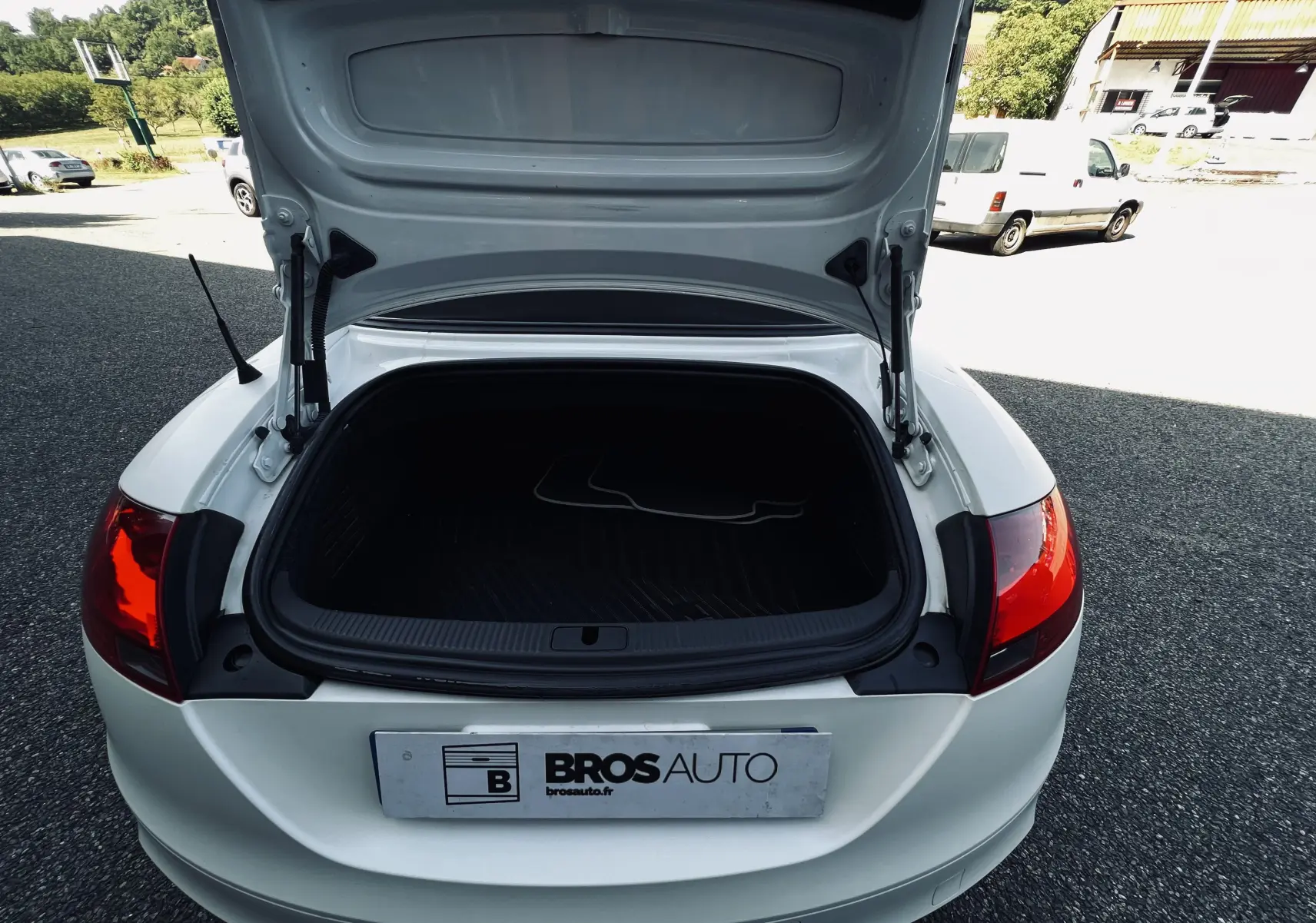 Coffre ouvert vu de l'arrière d'une Audi TT RS Roadster cabriolet blanc avec feux arrière rouges visibles.