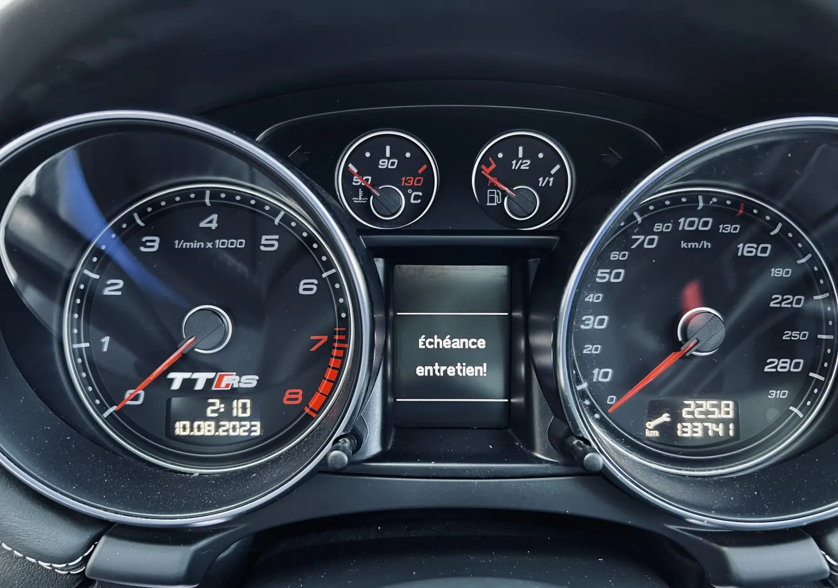 Vue rapprochée du tableau de bord de l'Audi TT RS avec compte-tours, vitesse et message d'entretien affiché.