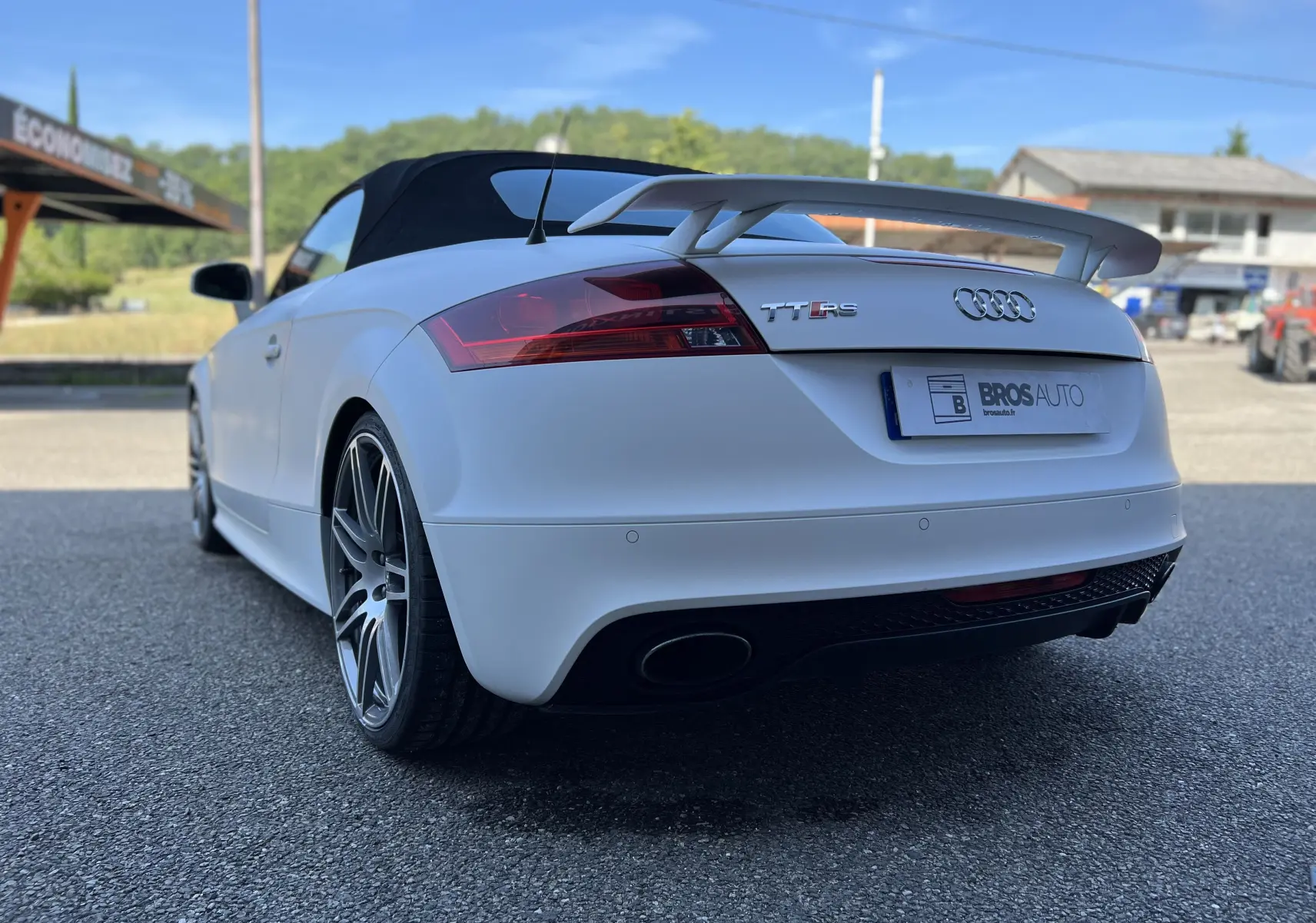 Audi TT RS Roadster blanc vue 3/4 arrière droit, capote noire et aileron sport bien visibles.