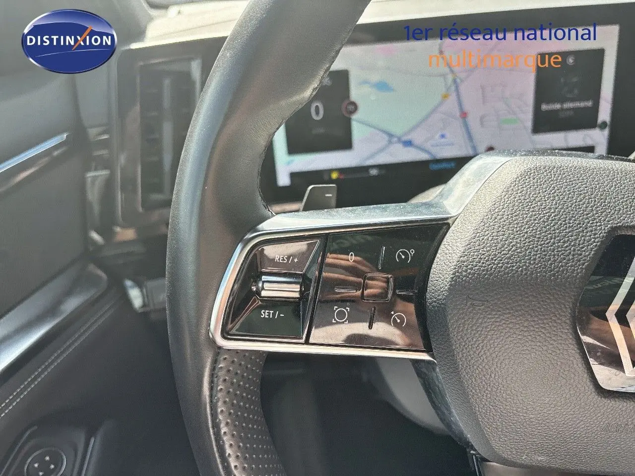 Gros plan sur le volant noir perforé du Renault Austral 2024 avec commandes intégrées et écran de navigation en arrière-plan.