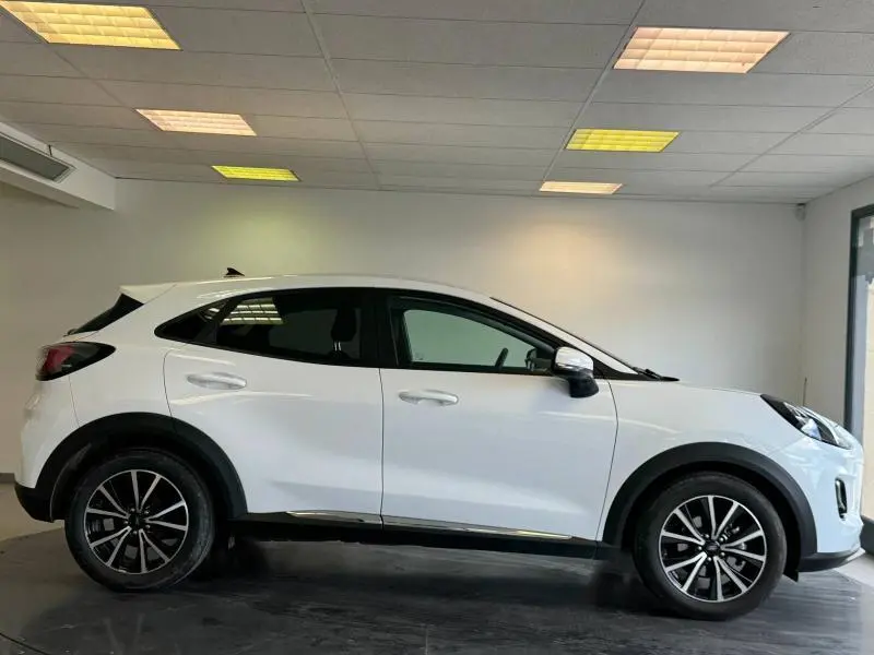 Vue de profil côté gauche d'un Ford Puma blanc glacier avec jantes noires et vitres arrière surteintées dans un showroom.