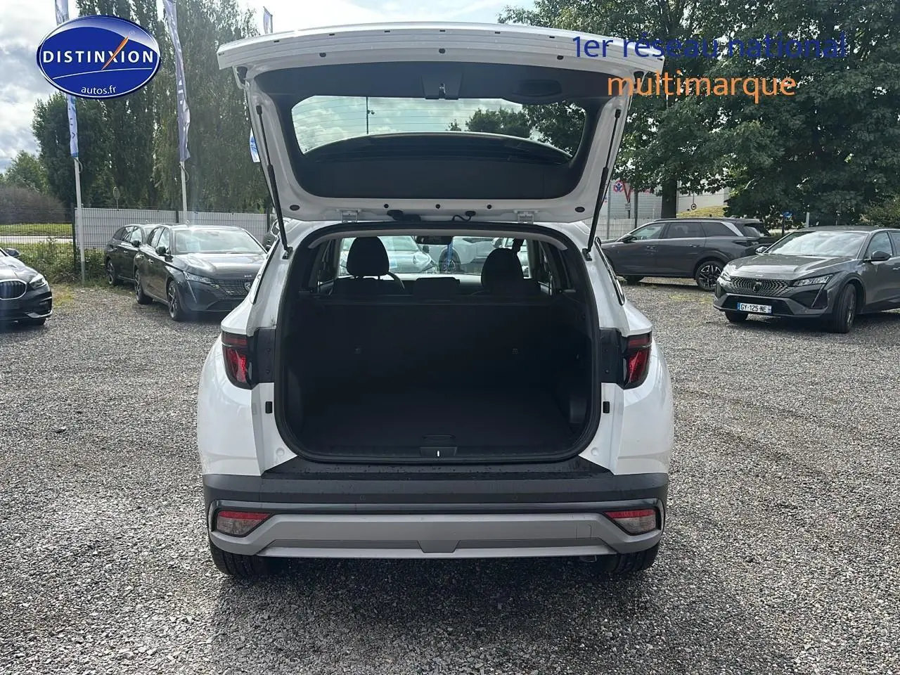 Vue arrière d'un Hyundai Tucson blanc sérénité avec coffre ouvert sur un parking extérieur.