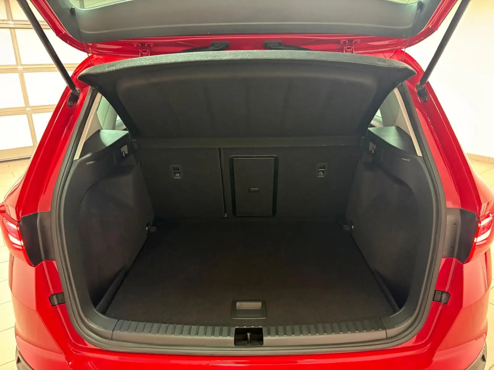Coffre ouvert vu de l'arrière d'un SEAT Ateca 2024 Rouge Velvet avec plancher à double fond visible.