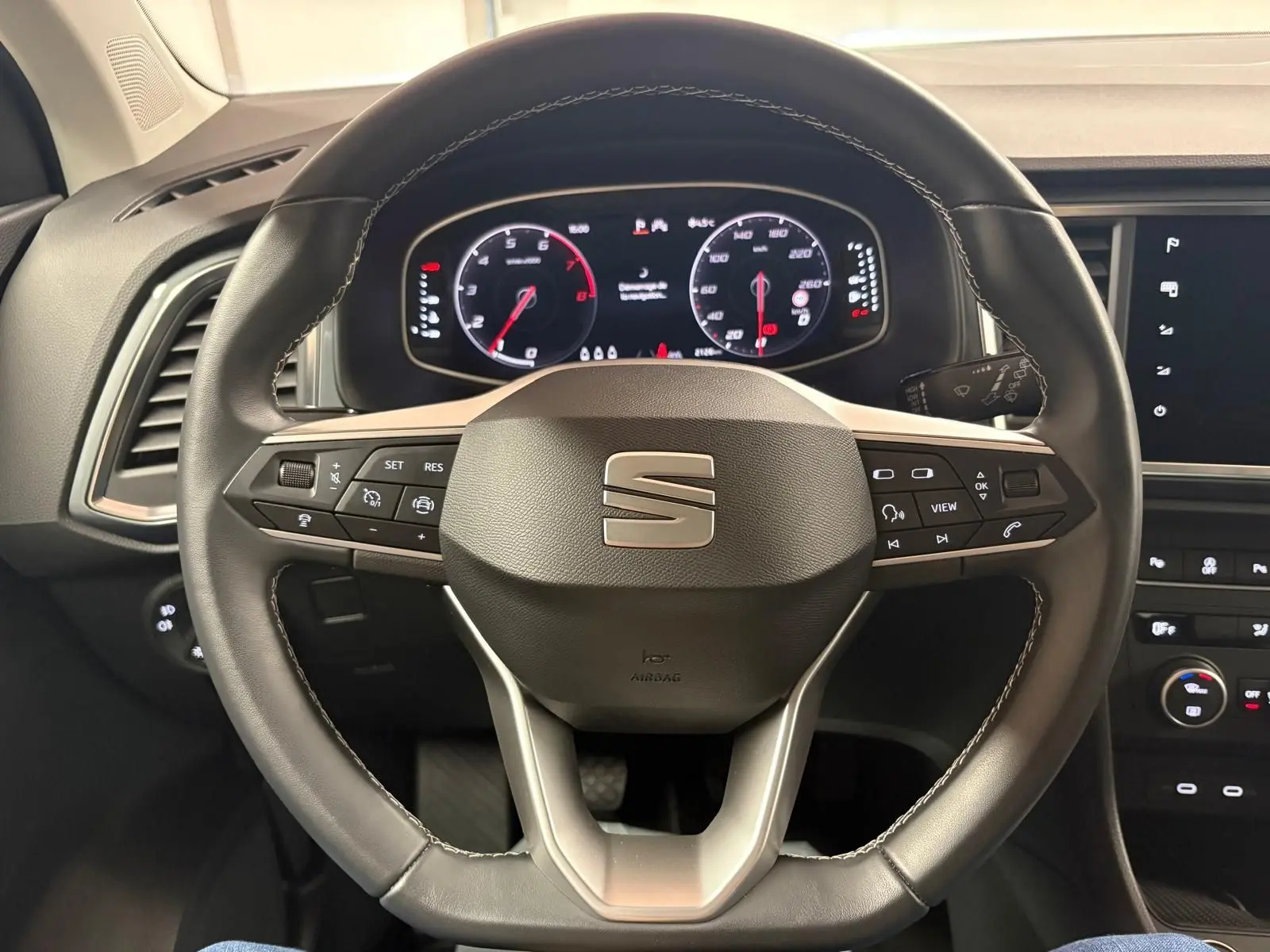 Vue rapprochée du volant noir du SEAT Ateca 2024 avec commandes intégrées et tableau de bord numérique allumé.