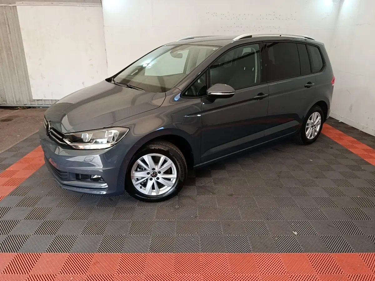 Volkswagen Touran gris clair vu en 3/4 avant droit, avec jantes alliage et vitres teintées.