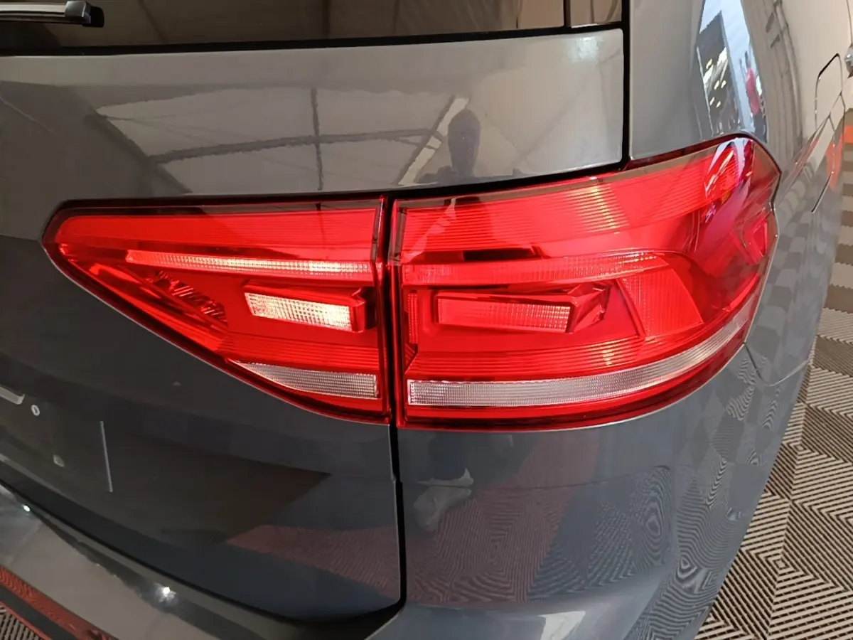 Gros plan sur le feu arrière droit rouge d’un Volkswagen Touran gris clair 2024, avec carrosserie brillante.