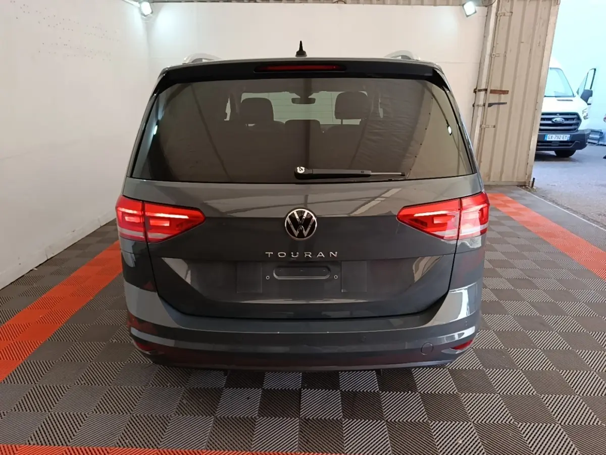 Vue arrière d’un Volkswagen Touran gris clair 2024 avec feux arrière allumés dans un garage.
