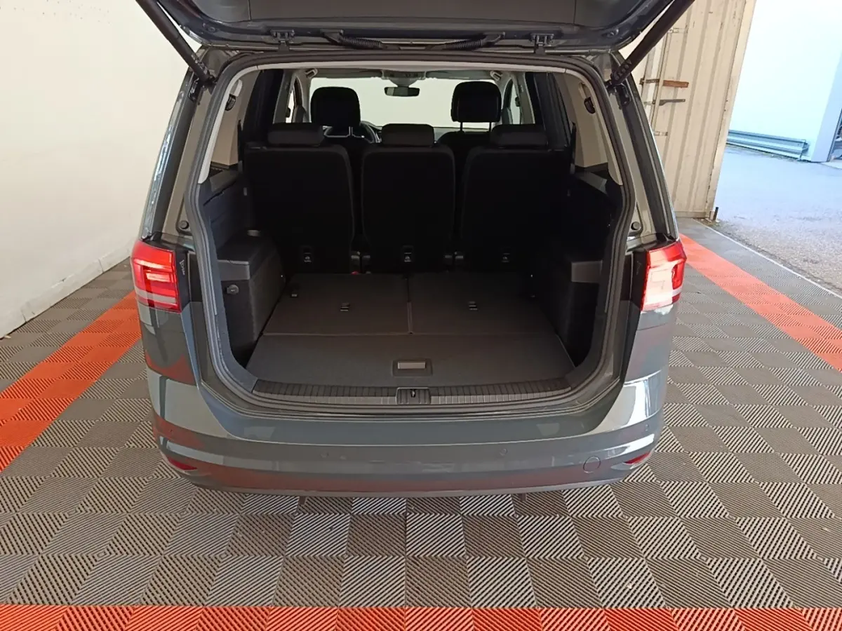 Vue arrière ouverte du Volkswagen Touran gris clair 2024, montrant le coffre spacieux avec sièges rabattus.