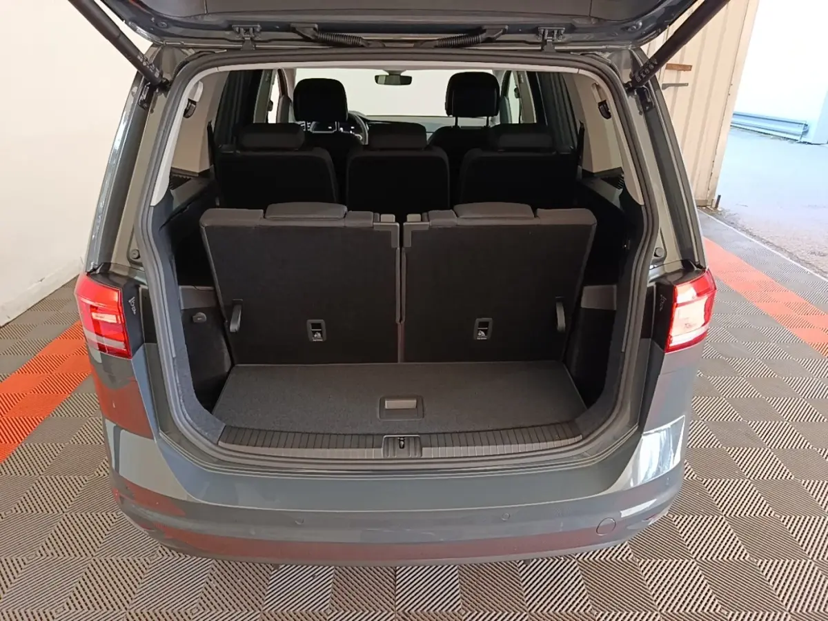 Vue arrière du coffre ouvert d'un Volkswagen Touran gris clair 2024 avec sièges arrière en position verticale.