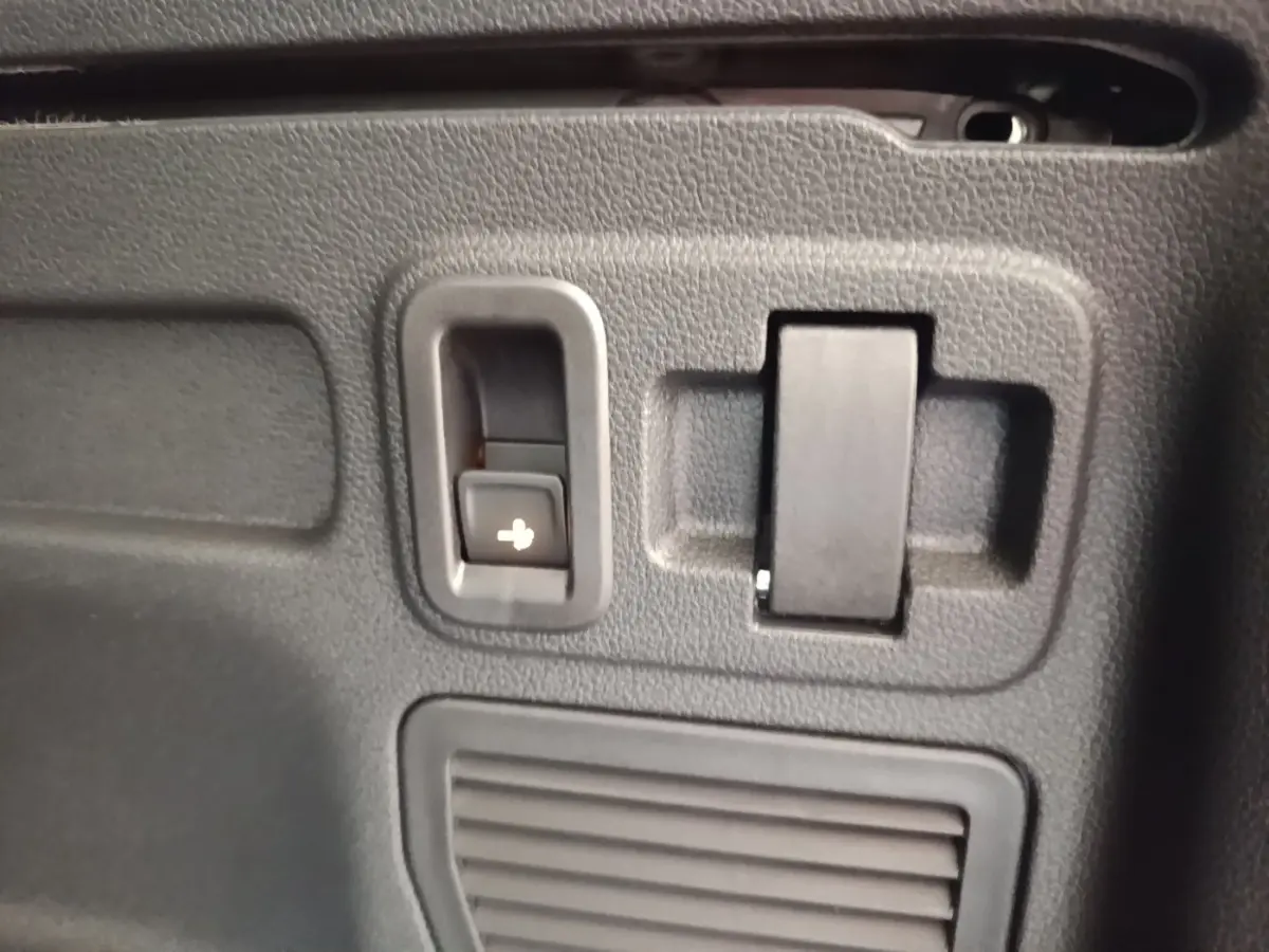 Détail intérieur montrant un bouton de rabattement des sièges dans le coffre du Volkswagen Touran gris clair 2024.