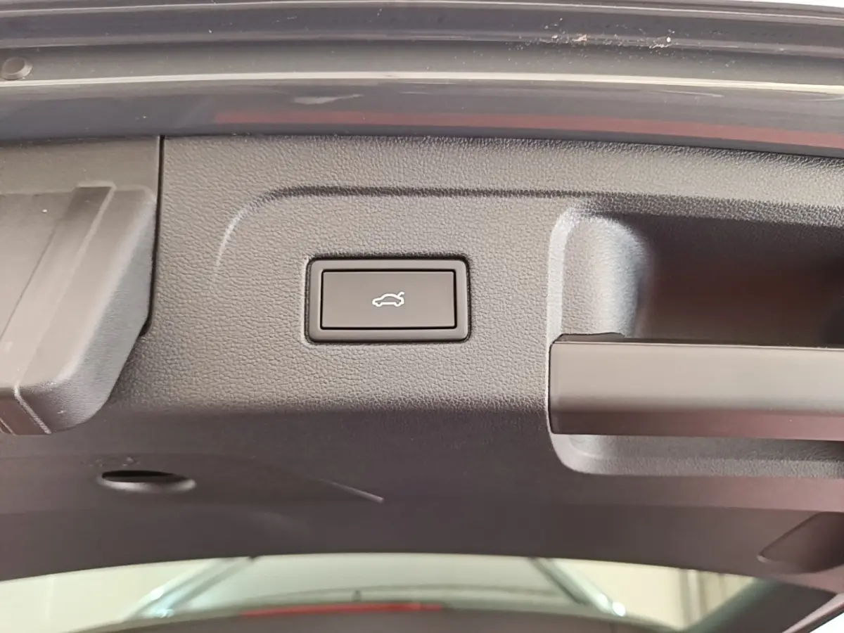 Bouton d'ouverture électrique du coffre sur la partie intérieure du hayon d'un Volkswagen Touran gris clair.